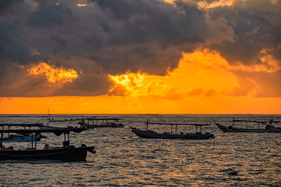 Vibrant sunset over traditional fishing boats in Bali, Indonesia.