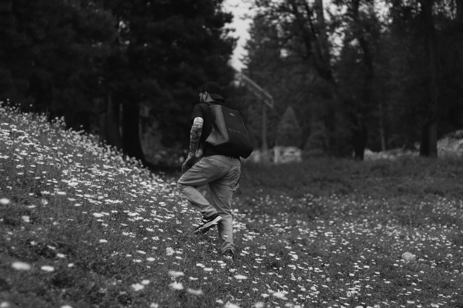 A man with a backpack hikes through a flower-covered meadow in a forest.