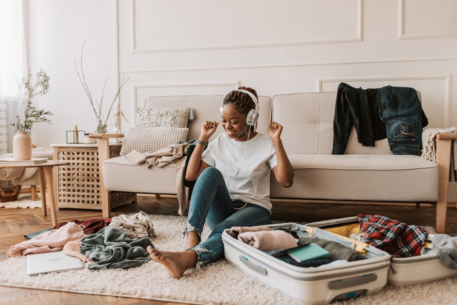 A cheerful woman listening to music while packing a suitcase in a cozy living room setting.