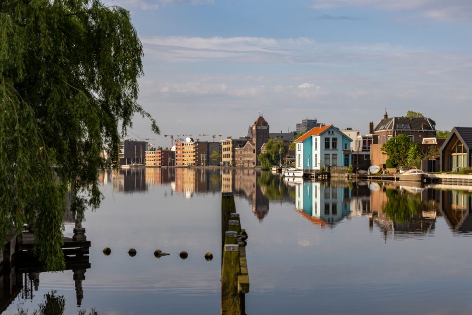 Scenic view of Amsterdam's canal with historic buildings reflected in calm water under a sunny sky.