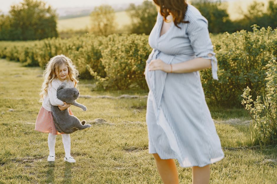 Pregnant mother and daughter enjoying a sunny day in a field with a toy.