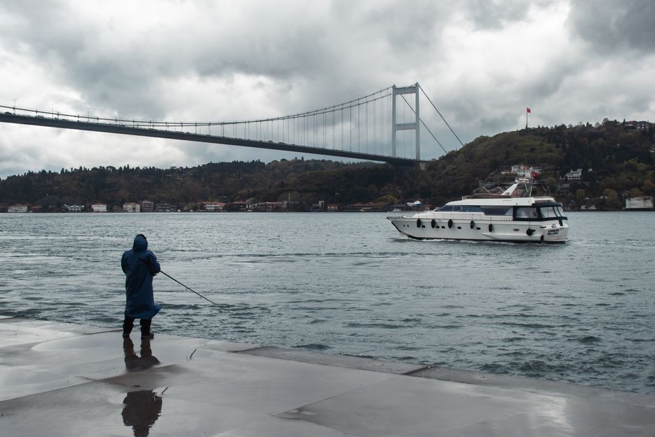 Man fishing by the Bosphorus with bridge and boat in İstanbul, Türkiye.