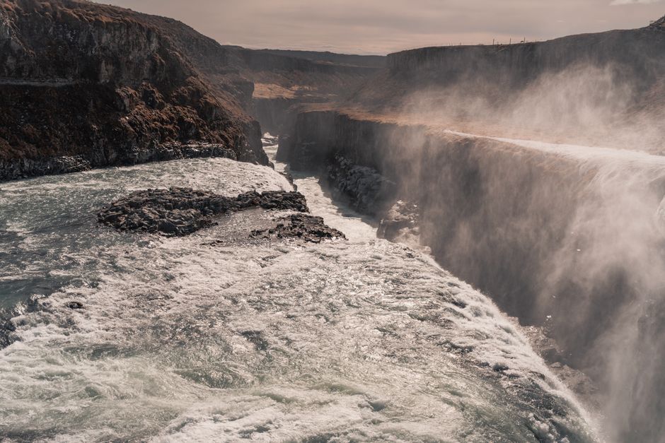 Stunning aerial view of a waterfall cascading through a canyon, showcasing Iceland's dramatic landscape.
