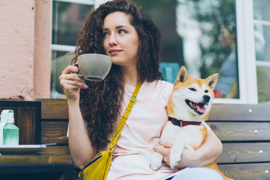Young woman relaxing with her Shiba Inu dog at a cozy outdoor café, enjoying a cup of coffee.