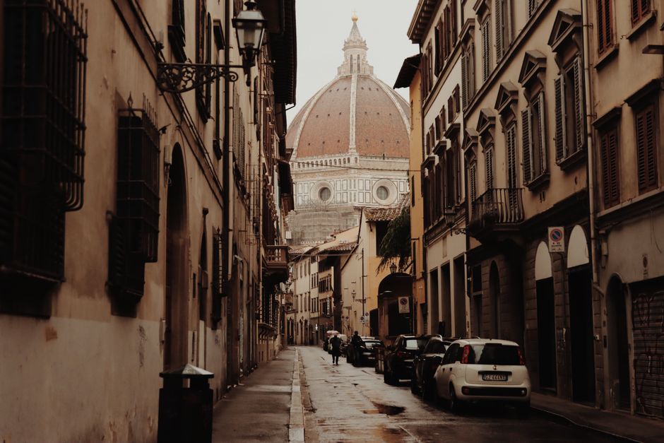 Historic Florence street scene featuring cars and Il Duomo in the backdrop on a rainy day.